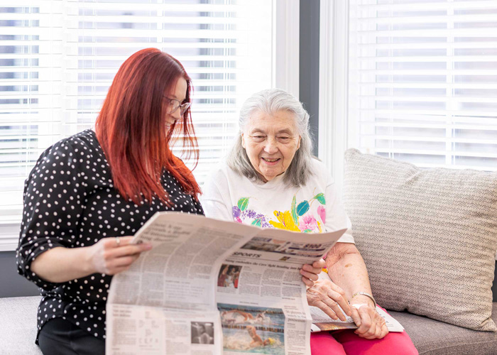 A resident and an employee sharing a moment together, reading the newspaper and enjoying each other's company in a bright, sunny room.