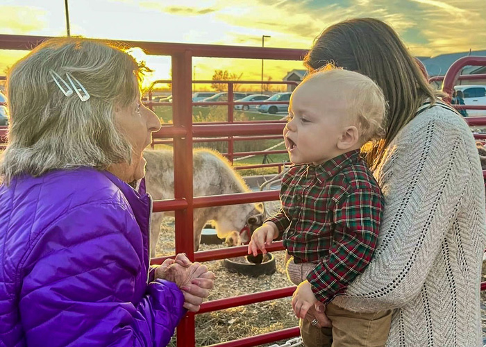 Senior resident interacting with a young child at a Christmas tree lighting event with a reindeer in the background during sunset.