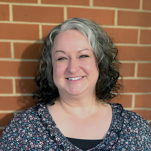 Rachel Ray, Resident Services Director at The Montvale Senior Living, smiles warmly in front of a brick wall, showcasing her welcoming presence in the community.