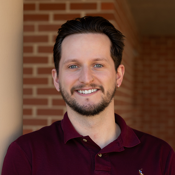 Brady Cummings, Senior Living Director at Montvale Senior Living, smiling confidently while standing near a pillar in front of a brick wall, dressed in a maroon polo.