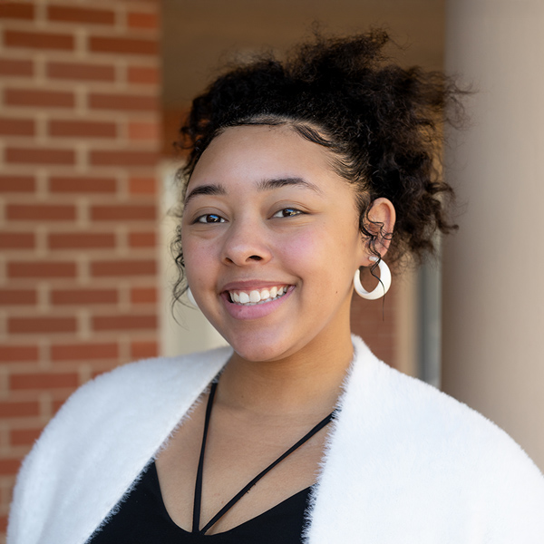 Bree Roberts, Senior Living Coordinator at Montvale Senior Living, smiling warmly while wearing a white sweater and hoop earrings, standing near a brick wall.