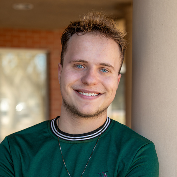 Logan Adkins, Operations Coordinator at Montvale Senior Living, smiling while standing near a pillar outside the community, wearing a green shirt with a striped collar.