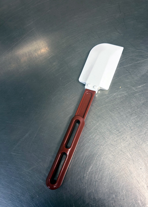 Rubber spatula with a white flexible blade and red handle resting on a stainless steel countertop, ideal for scraping bowls and reducing food waste in the kitchen.