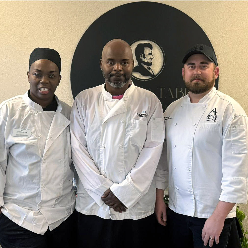 Three members of the Montvale Culinary team smile proudly in front of the community's restaurant sign.